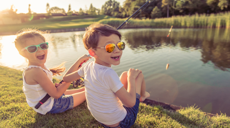 Two children fishing from a grassy lake bank at sunset